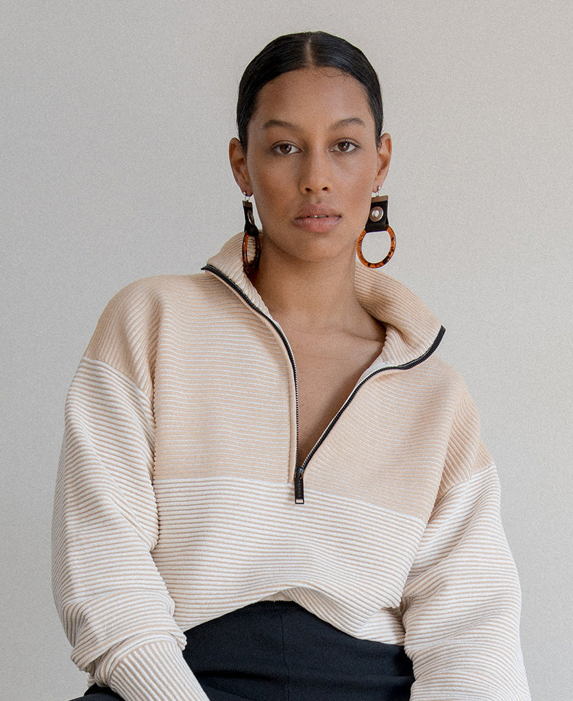 Female model wears the Nagnata Zhen Zip Thru Sweater in sandstone and cream.